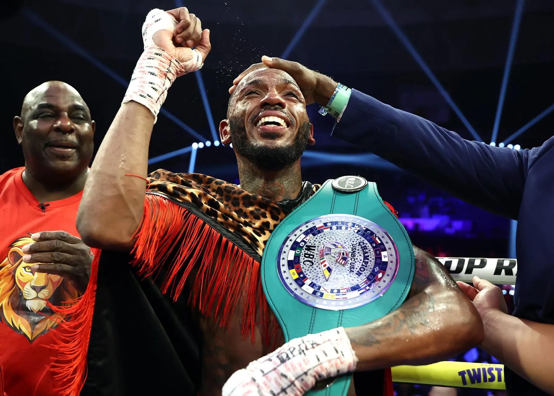Nahir Albright celebrates with a championship belt as his team surrounds him in the ring.