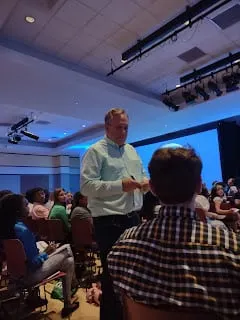 Tom Jackman speaks with students in a crowded, dimly lit auditorium.