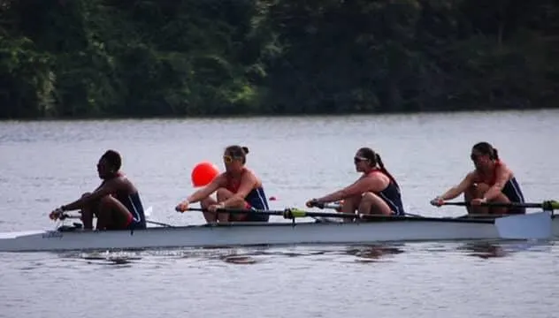 A women's four rows on a calm, tree-lined river.